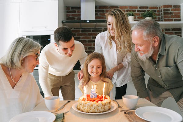 A joyful family gathered around a birthday cake to celebrate a young girl's fifth birthday.