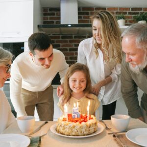 A joyful family gathered around a birthday cake to celebrate a young girl's fifth birthday.